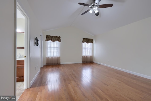 empty room with light wood finished floors, baseboards, lofted ceiling, ceiling fan, and a sink