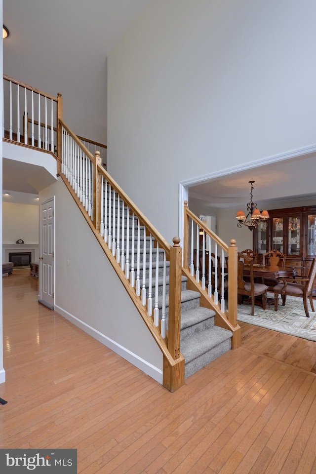 stairway featuring a chandelier, baseboards, a towering ceiling, and hardwood / wood-style floors