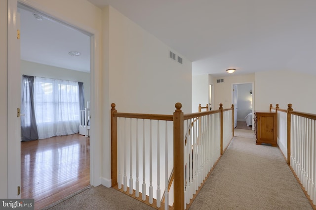 corridor featuring an upstairs landing, visible vents, and light colored carpet