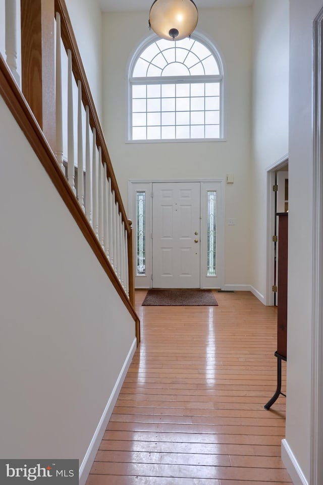 foyer with baseboards, a towering ceiling, hardwood / wood-style floors, and stairs