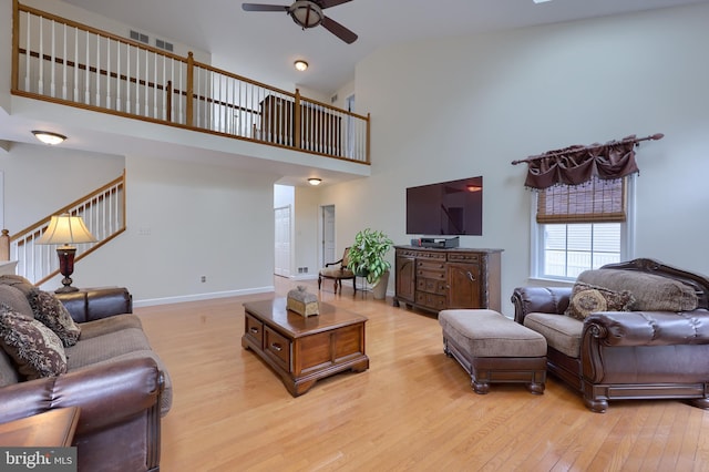 living room with light wood finished floors, stairway, ceiling fan, high vaulted ceiling, and baseboards