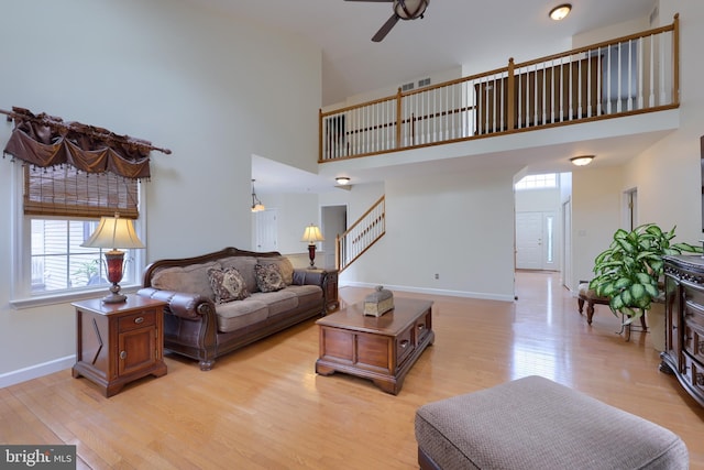 living area with light wood-style flooring, a towering ceiling, stairway, ceiling fan, and baseboards