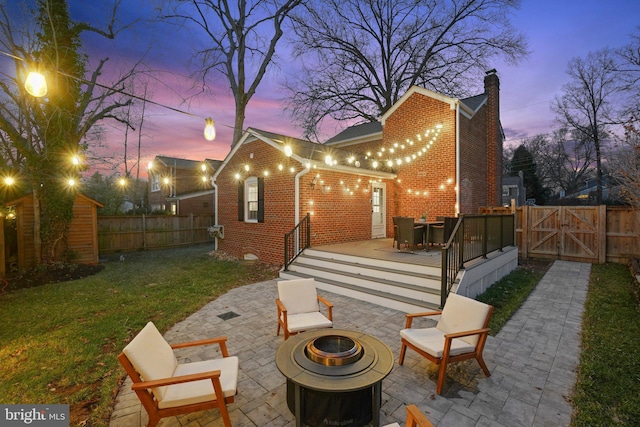 back house at dusk with a yard, a patio area, and a fire pit