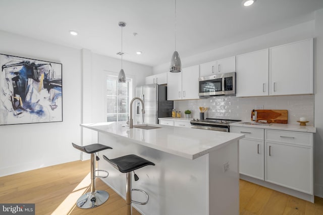 kitchen with white cabinetry, decorative light fixtures, a center island with sink, stainless steel appliances, and light hardwood / wood-style floors