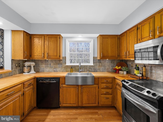 kitchen with light wood-style flooring, a sink, backsplash, butcher block countertops, and appliances with stainless steel finishes