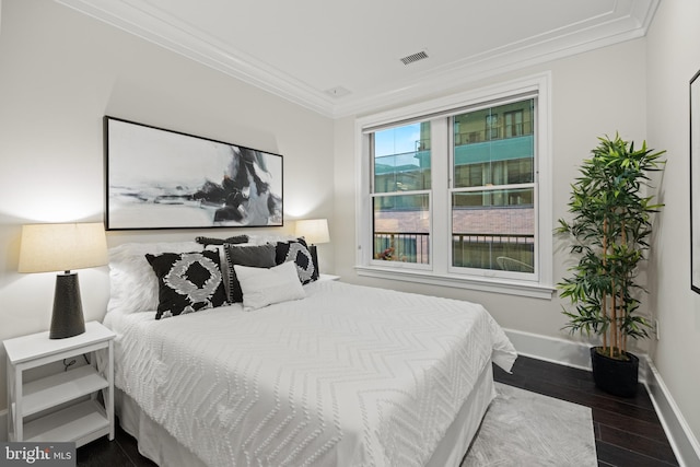 bedroom with ornamental molding, visible vents, baseboards, and wood finished floors