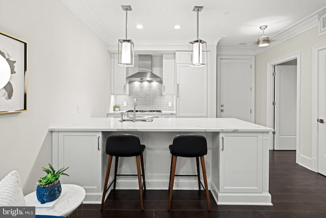 kitchen featuring light stone counters, white cabinets, hanging light fixtures, and wall chimney range hood