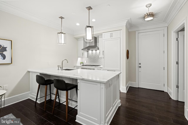 kitchen featuring white cabinets, decorative light fixtures, a sink, and wall chimney range hood