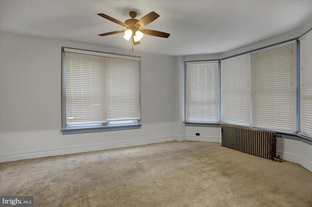 carpeted empty room featuring ceiling fan and radiator