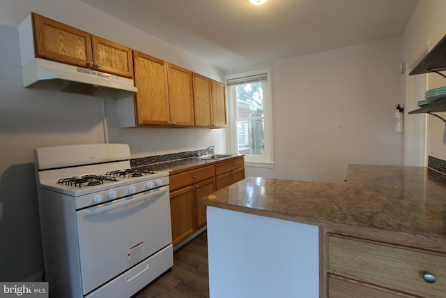 kitchen with dark countertops, white gas stove, under cabinet range hood, a peninsula, and a sink