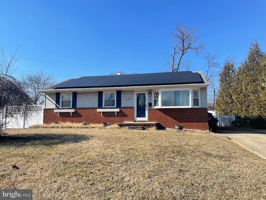 view of front of home featuring roof mounted solar panels, a front yard, fence, and brick siding