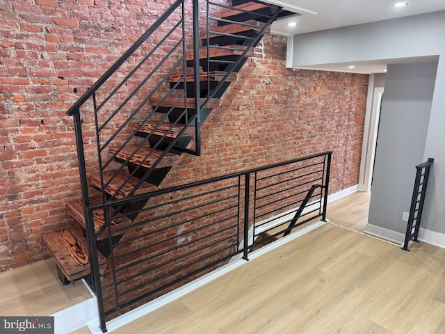 staircase featuring brick wall and hardwood / wood-style floors