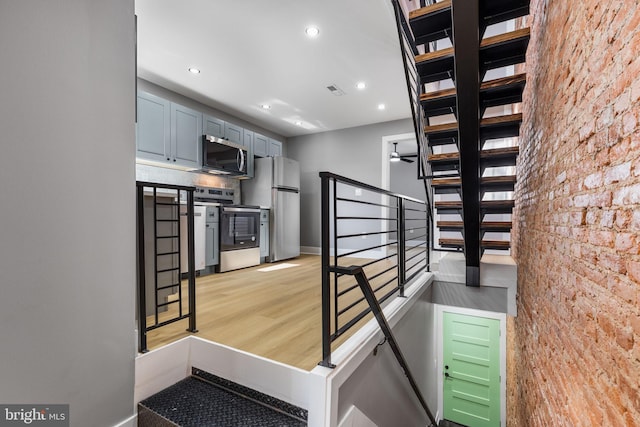 staircase with wood-type flooring, brick wall, and ceiling fan