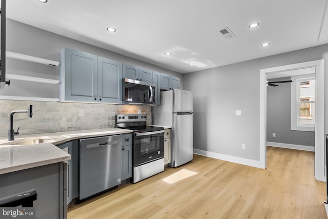 kitchen featuring appliances with stainless steel finishes, sink, decorative backsplash, light stone countertops, and light hardwood / wood-style flooring