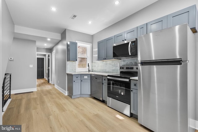 kitchen with tasteful backsplash, appliances with stainless steel finishes, sink, and light wood-type flooring