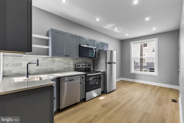 kitchen with sink, light stone counters, light hardwood / wood-style flooring, appliances with stainless steel finishes, and backsplash