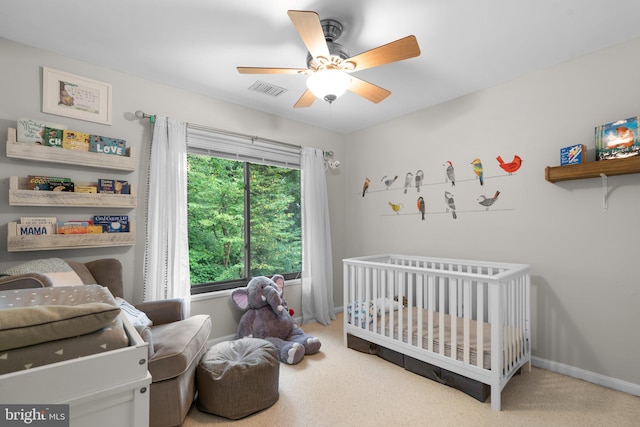 carpeted bedroom featuring a crib and ceiling fan