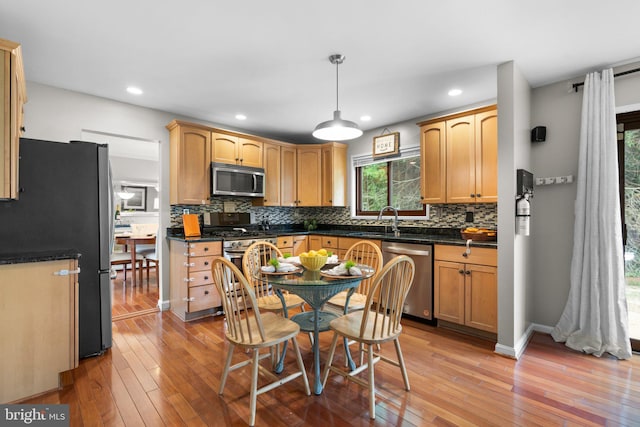 kitchen with sink, light hardwood / wood-style flooring, appliances with stainless steel finishes, hanging light fixtures, and decorative backsplash