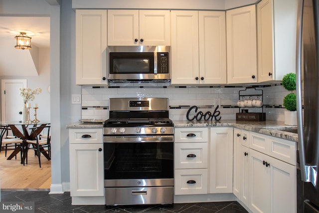 kitchen with light stone counters, stainless steel appliances, backsplash, and white cabinets