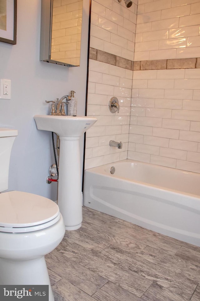 bathroom with wood-type flooring, toilet, and tiled shower / bath combo