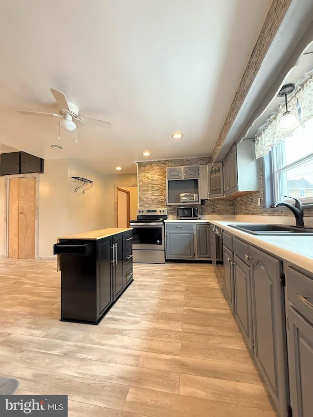 kitchen with stainless steel electric range oven, sink, backsplash, ceiling fan, and light hardwood / wood-style flooring