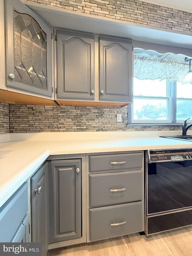 kitchen featuring sink, gray cabinets, backsplash, black dishwasher, and light wood-type flooring