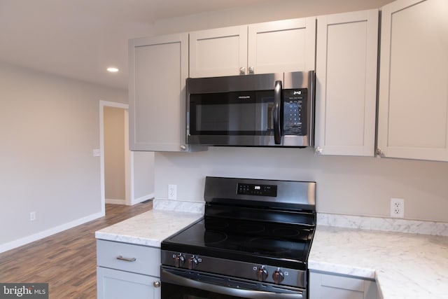 kitchen with wood-type flooring, appliances with stainless steel finishes, white cabinets, and light stone counters