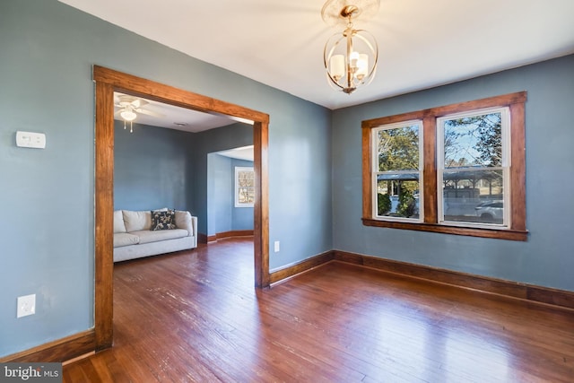 empty room with a wealth of natural light, an inviting chandelier, baseboards, and wood finished floors