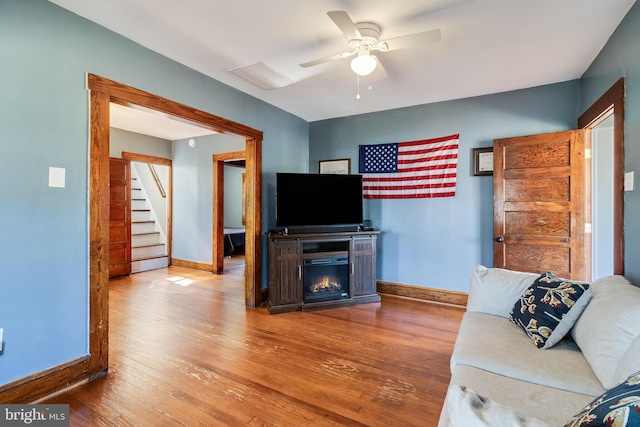 living room featuring ceiling fan, baseboards, a lit fireplace, and wood finished floors