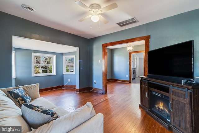 living area with visible vents, ceiling fan, baseboards, and wood-type flooring