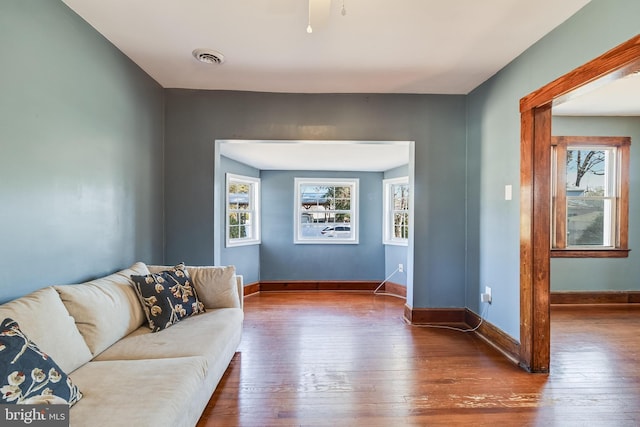 living room with hardwood / wood-style floors, visible vents, baseboards, and a ceiling fan