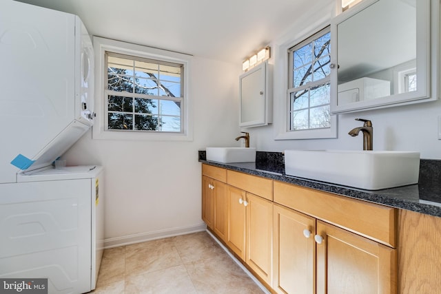 full bath featuring double vanity, baseboards, stacked washer and clothes dryer, and a sink