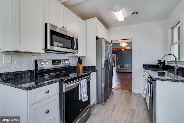 kitchen with stainless steel appliances, dark stone counters, light wood-style floors, white cabinets, and decorative backsplash