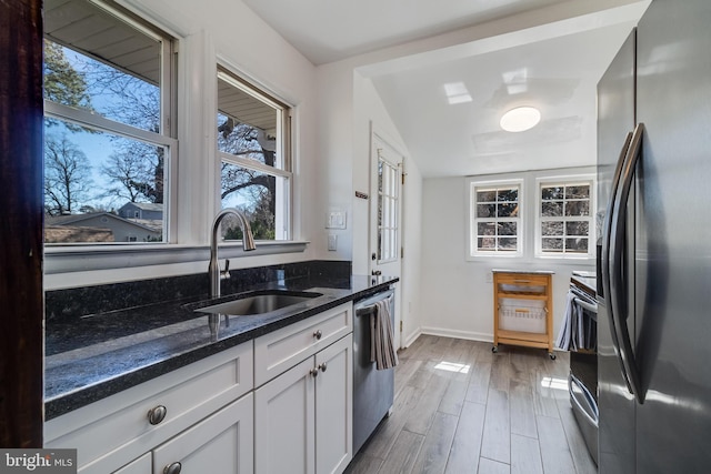 kitchen featuring a sink, stainless steel appliances, a healthy amount of sunlight, and dark stone counters