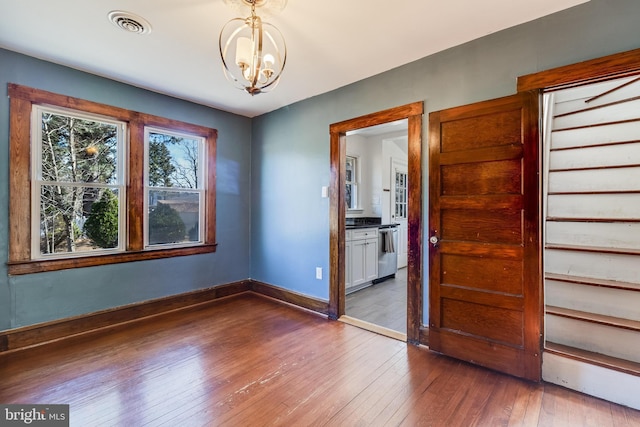 unfurnished room with an inviting chandelier, baseboards, visible vents, and wood-type flooring