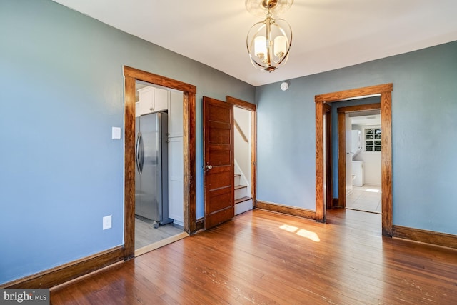 unfurnished bedroom featuring baseboards, freestanding refrigerator, a notable chandelier, wood-type flooring, and a baseboard radiator