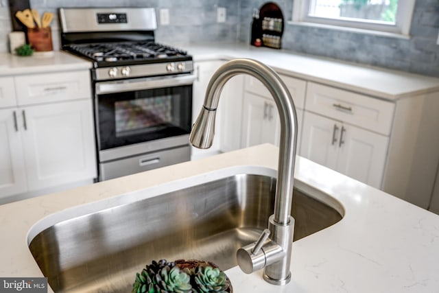 room details featuring white cabinetry, stainless steel range with gas stovetop, light stone countertops, and sink