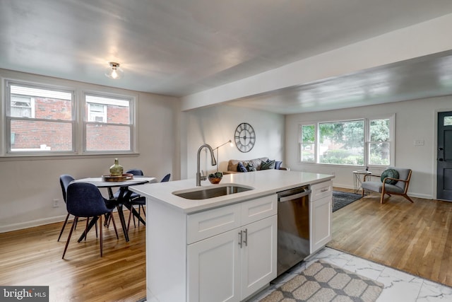 kitchen with white cabinetry, sink, stainless steel dishwasher, light hardwood / wood-style floors, and a center island with sink