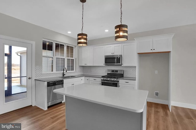 kitchen with sink, white cabinetry, appliances with stainless steel finishes, a kitchen island, and pendant lighting