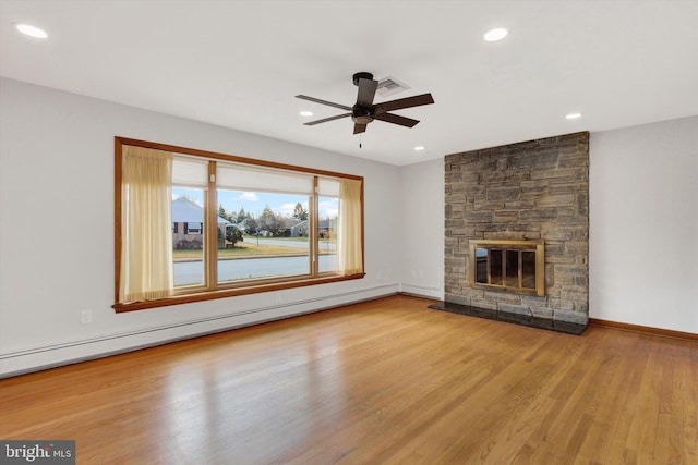 unfurnished living room featuring ceiling fan, a stone fireplace, a baseboard heating unit, and light hardwood / wood-style floors