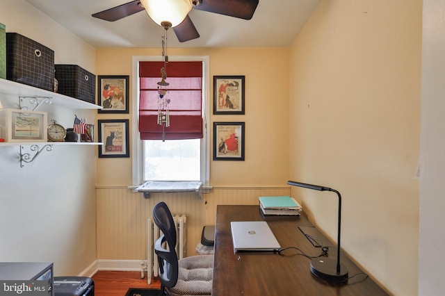 office featuring hardwood / wood-style floors, radiator heating unit, ceiling fan, and wood walls