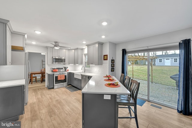 kitchen featuring gray cabinetry, stainless steel appliances, a peninsula, a kitchen breakfast bar, and light wood-style floors