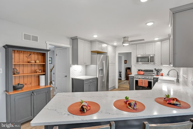 kitchen with visible vents, gray cabinetry, appliances with stainless steel finishes, a sink, and light stone countertops