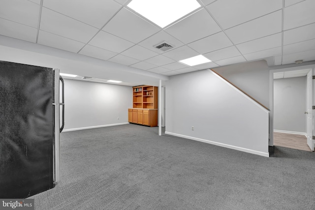 finished basement featuring carpet floors, visible vents, freestanding refrigerator, a drop ceiling, and baseboards