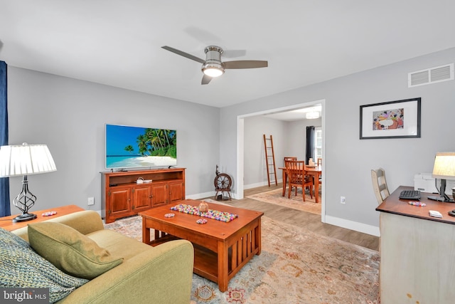 living room featuring light wood-style floors, baseboards, visible vents, and a ceiling fan