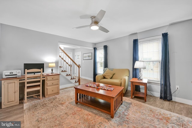 living area featuring light wood finished floors, stairs, baseboards, and a ceiling fan