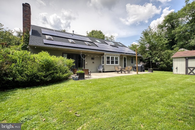 back of house with solar panels, a storage unit, a lawn, and a patio area