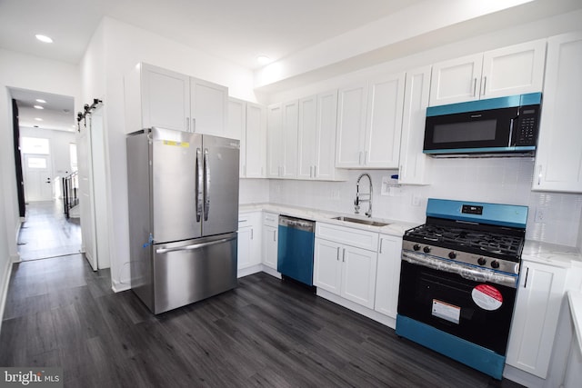 kitchen with appliances with stainless steel finishes, a barn door, sink, and white cabinets