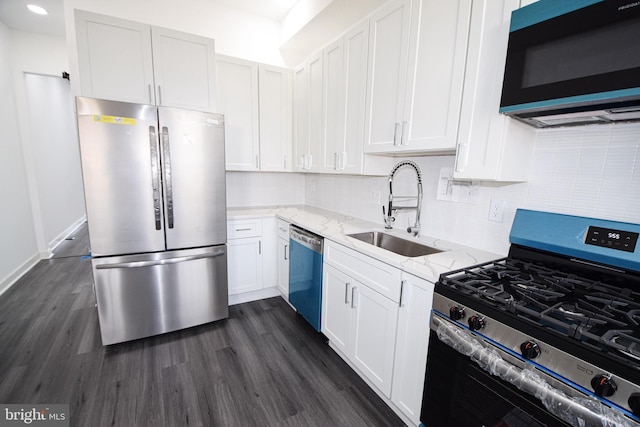 kitchen with sink, appliances with stainless steel finishes, white cabinetry, light stone counters, and dark hardwood / wood-style flooring