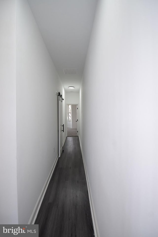 corridor with a barn door and dark wood-type flooring